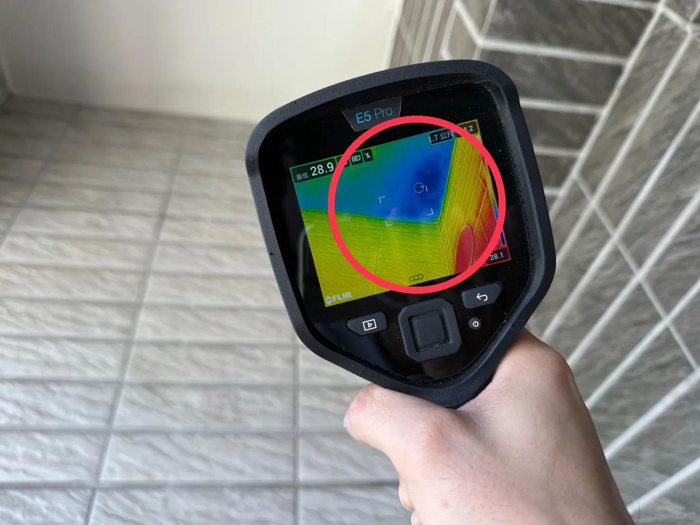 Main tenant une caméra thermique FLIR E5 Pro dont l’écran affiche l’image thermique d’un mur carrelé