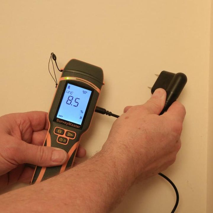 Mains tenant un humidimètre Protimeter Surveymaster relié à une sonde par un câble