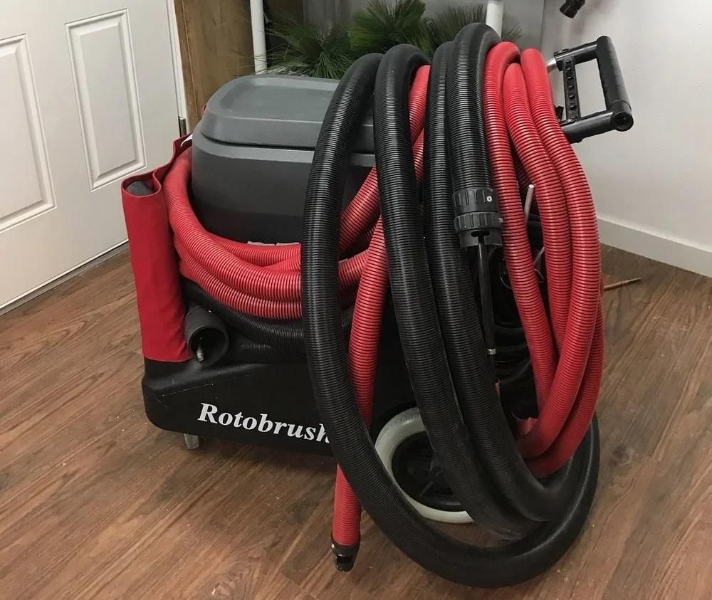 Machine Rotobrush aux flexibles noirs et rouges enroulés, posée sur un parquet